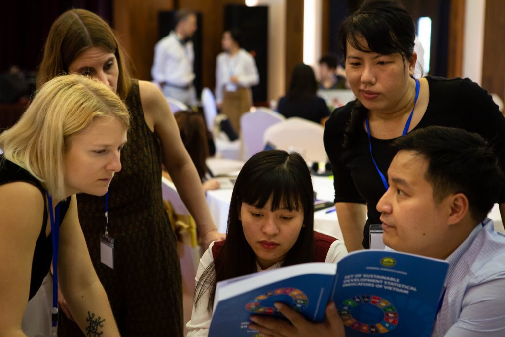 IRI staff and Vietnamese government officials share materials about the SDG2 goals; one official holds a book while others look over their shoulders.