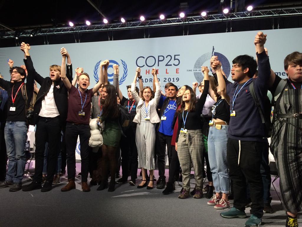 Young people stand on a stage holding hands during climate activist Greta Thunberg’s speech at COP25. 